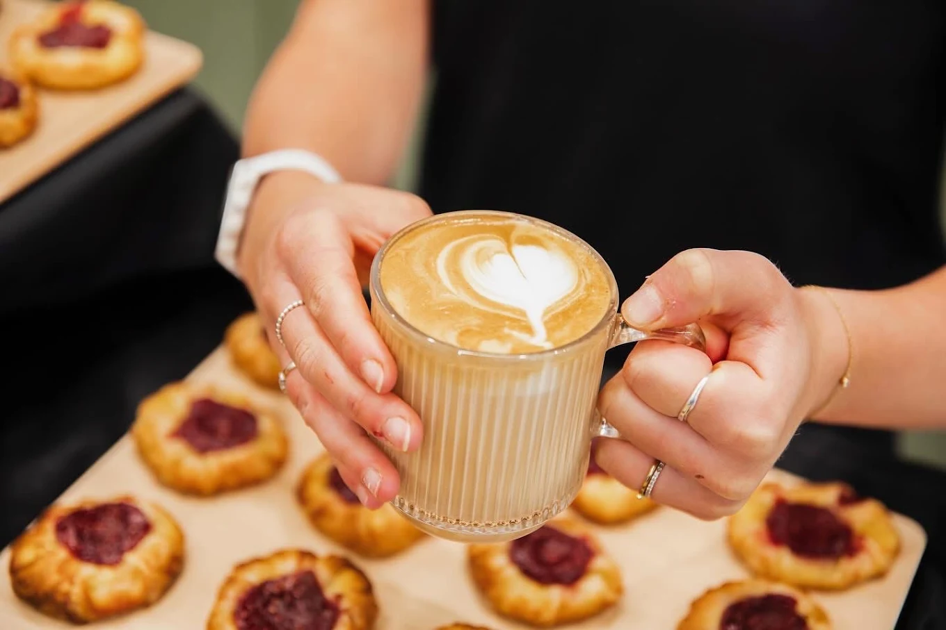 Un latté avec un cœur dessiné dans la mousse, tenu au-dessus d'un plateau de danoises aux petits fruits