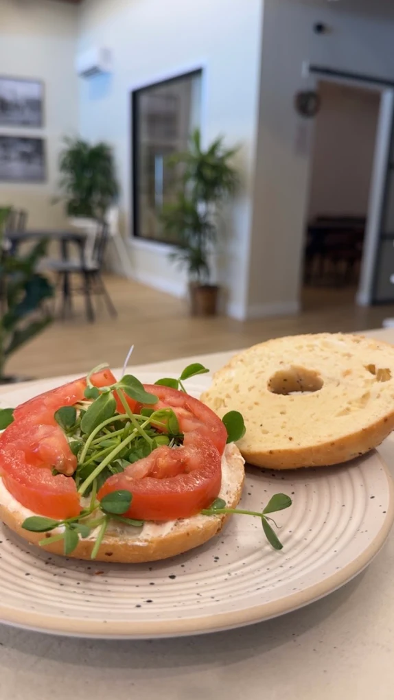 Bagel tartiné de fromage à la crème, garni de tranches de tomate et de pousses