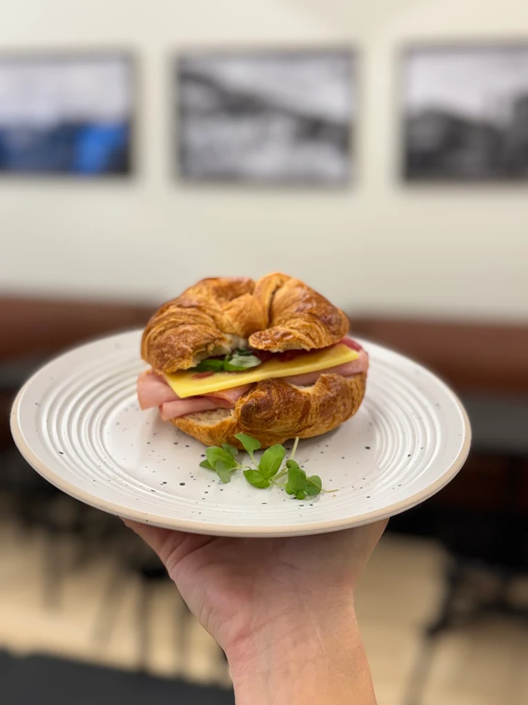 Croissant déjeuner garni de jambon, fromage et pousses, présenté dans une assiette
