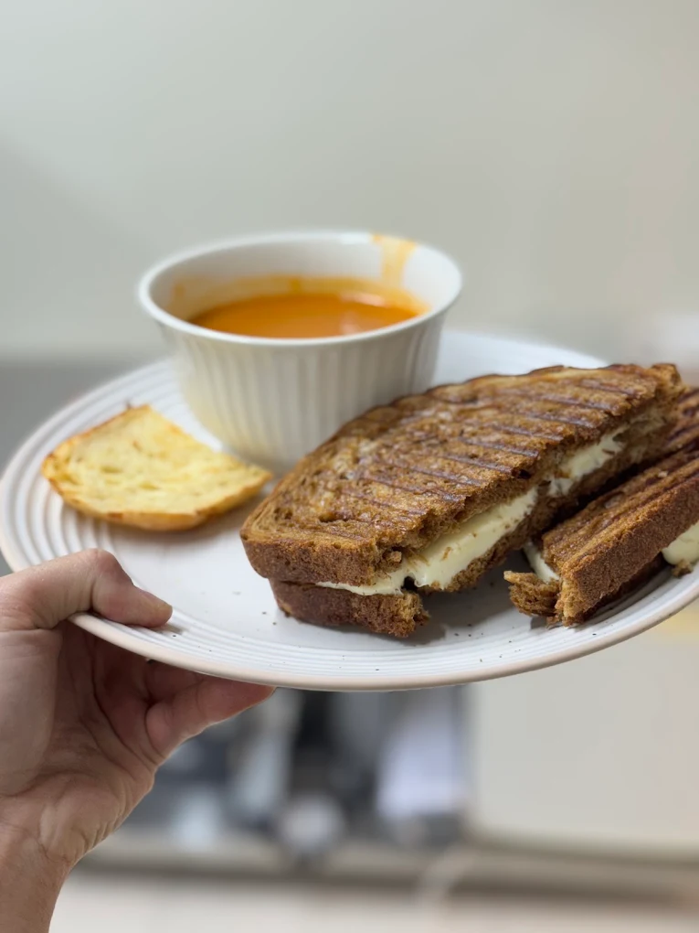Grilled cheese sur pain de grains, servi avec un bol de soupe et un morceau de pain