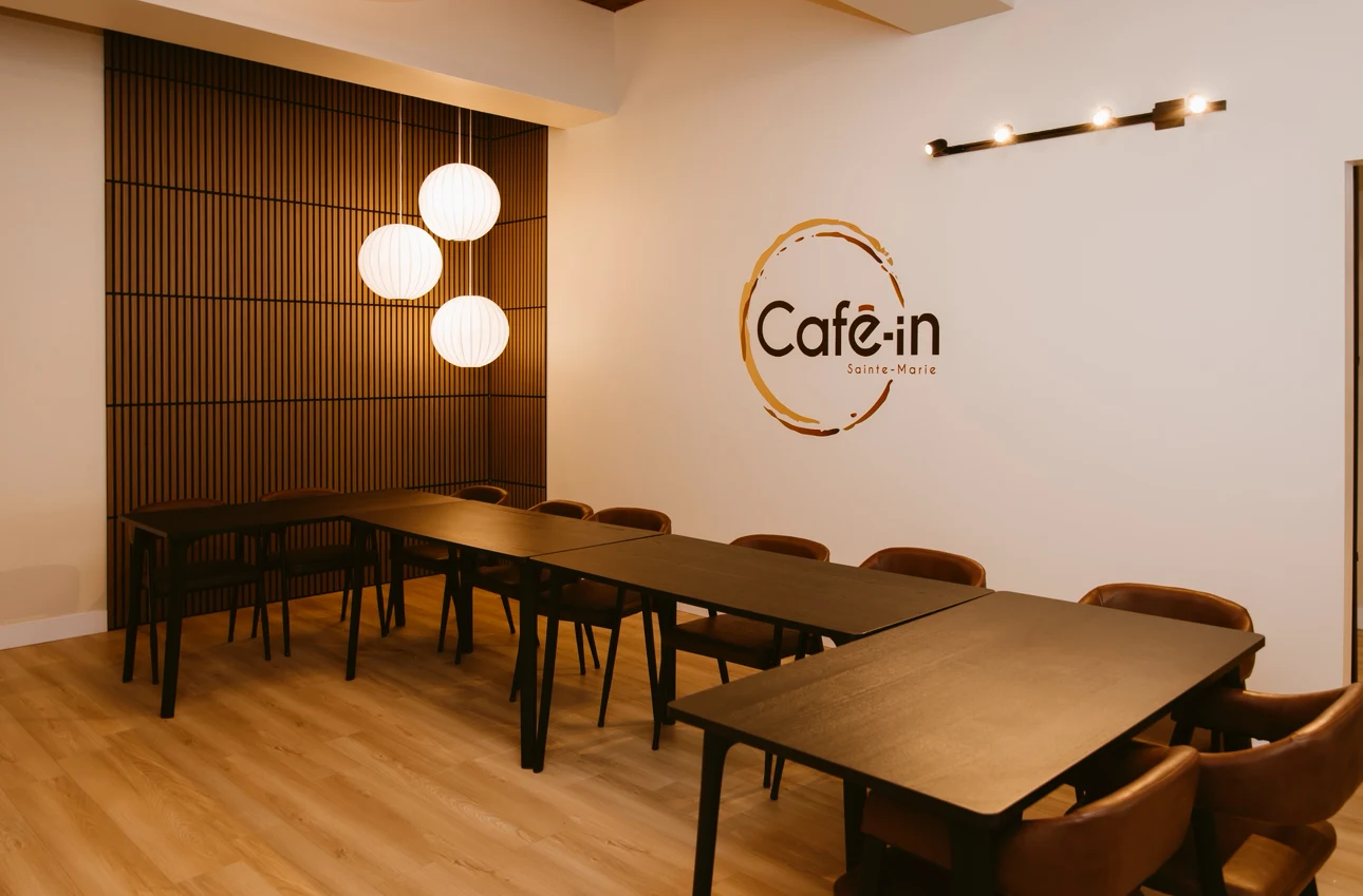 La salle privée du Café-in : longues tables foncées, chaises de cuir, luminaires ronds et logo au mur